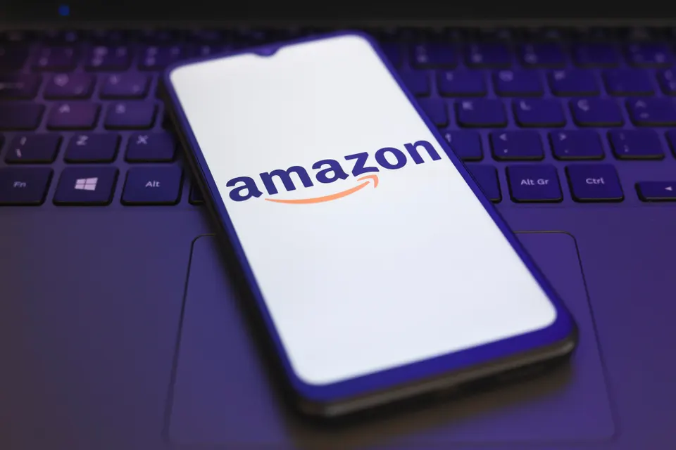 Amazon logo on smartphone sitting atop a laptop keyboard lit in dark purple. 