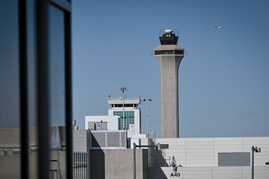 A plane takes off near an air traffic control tower at Denver International Airport. Some air traffic controllers have called out sick while others have chosen to retire.
