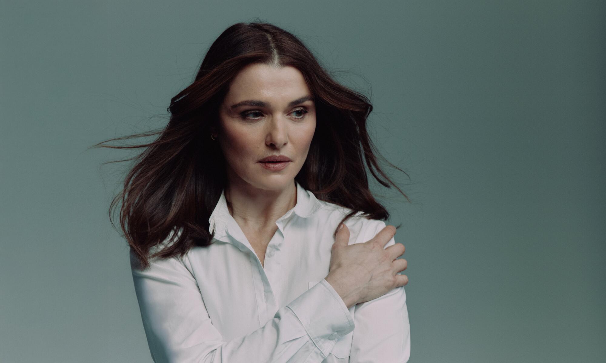 A woman with brown shoulder length hair in a white shirt with her hand placed on her shoulder.