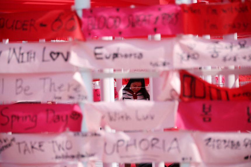 A BTS supporter is seen through messages written by others during a March 2026 event in Seoul to promote the group's new album.