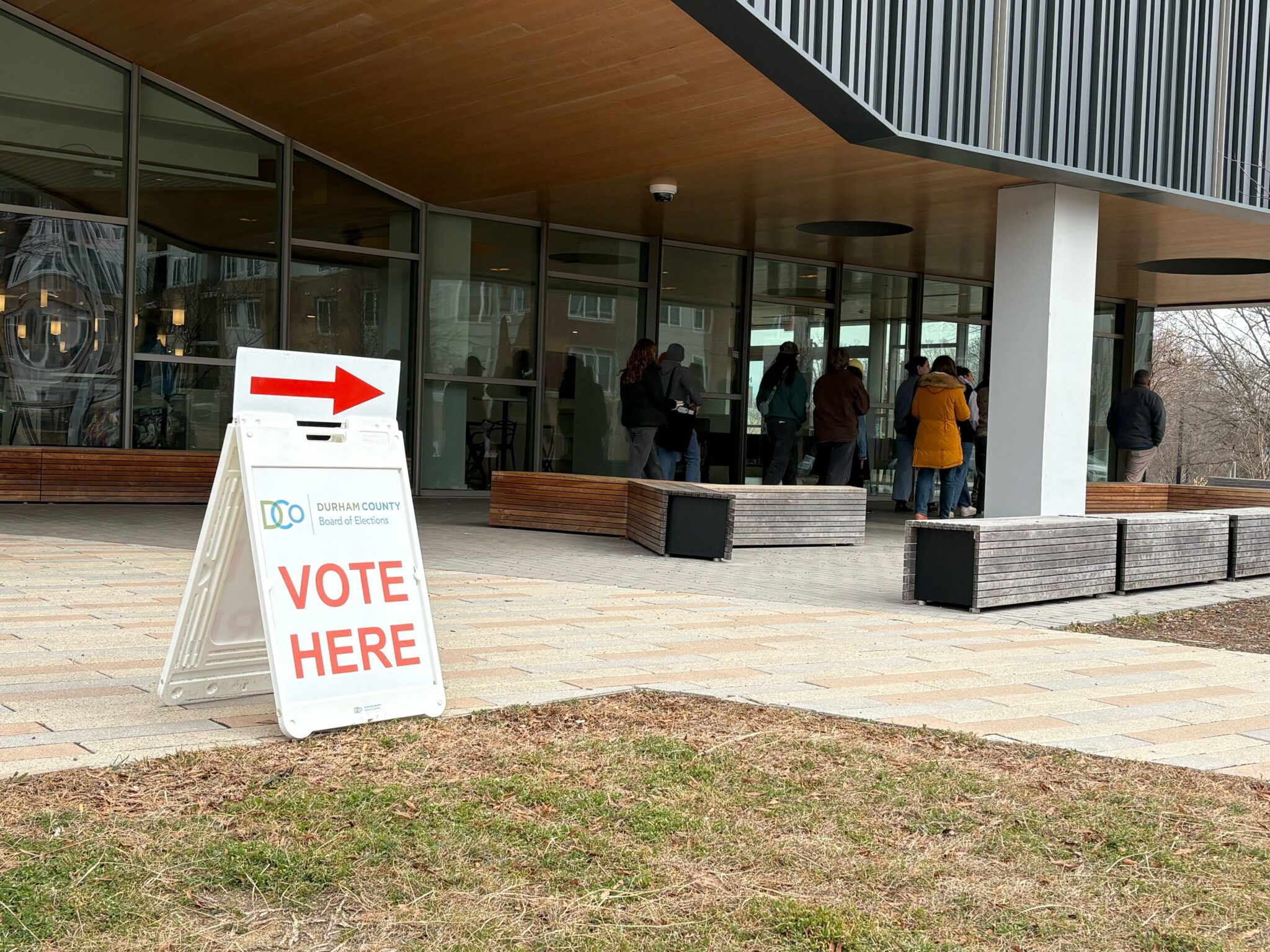 A line of voters queues up past a sign labeled "Vote Here."