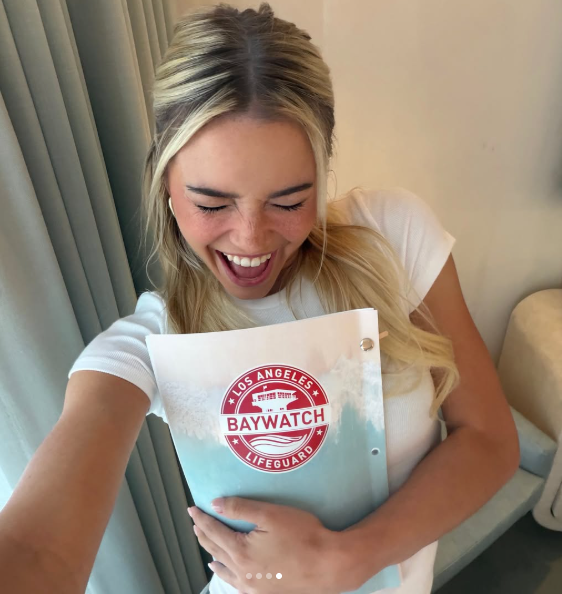 A young woman laughs while holding a "Los Angeles Baywatch Lifeguard" script.